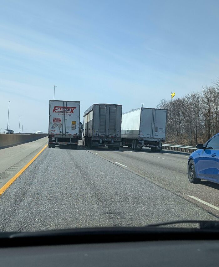 Three trucks blocking multiple lanes of a highway with a blue car trying to pass, illustrating dumb drivers on the road.