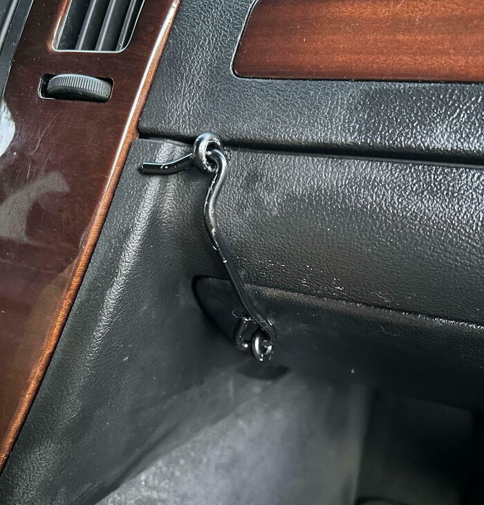 Car dashboard with a black metal hook used as a makeshift latch, an example of if it’s stupid but it works.