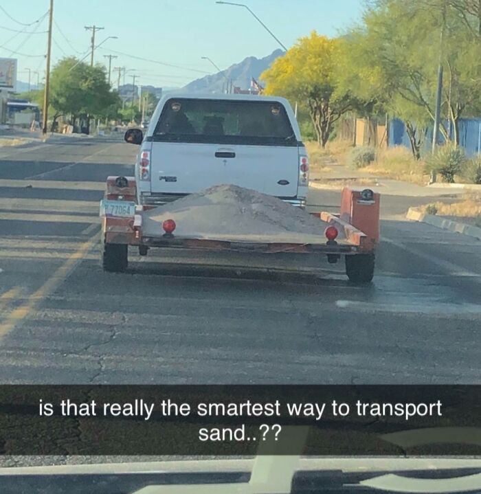 White pickup truck towing a trailer with loose sand piled high, an example of dumb drivers being shamed on the road.