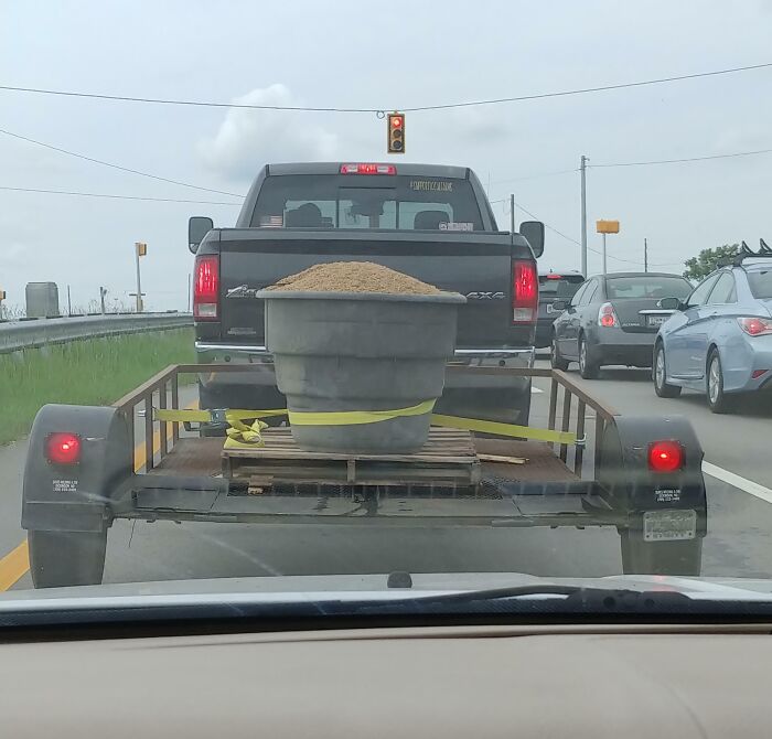 Truck towing unsecured large planter filled with sand on busy road, illustrating dumb drivers and unsafe driving behavior.