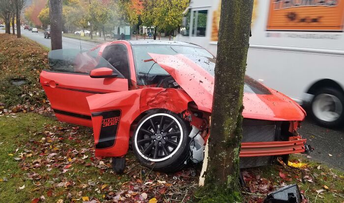 Red sports car crashed into a tree on a rainy road, illustrating reckless behavior by dumb drivers caught in accidents.
