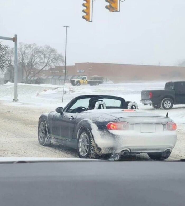 Convertible car covered in snow on icy road, illustrating dumb drivers caught in winter driving conditions.