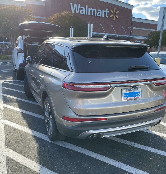 Silver Lincoln SUV illegally parked in handicap-striped area outside Walmart, example of dumb drivers shamed in new pics.