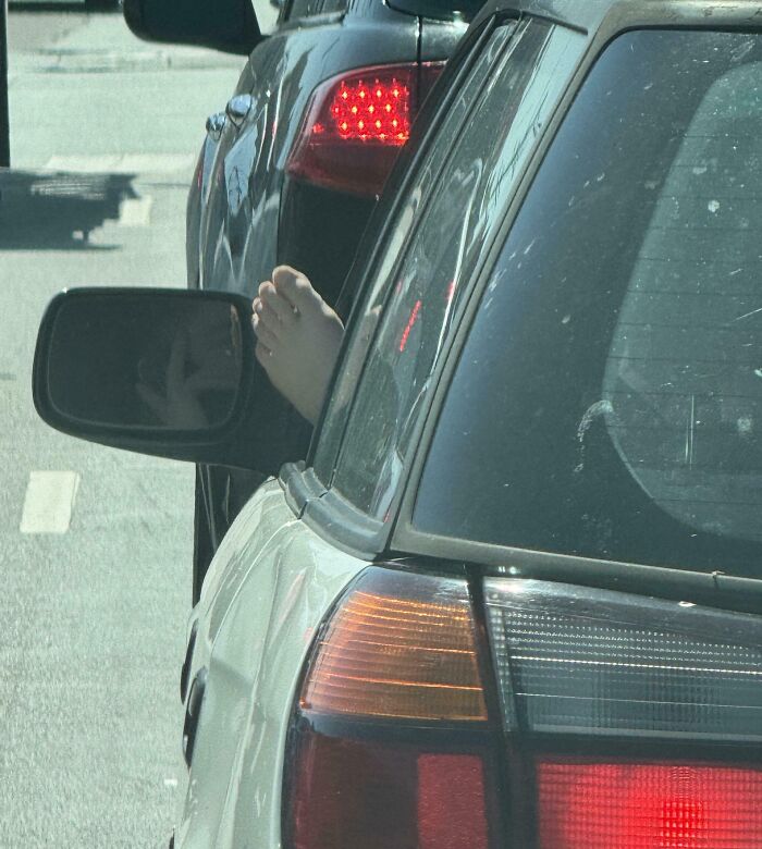A car with a person’s bare foot sticking out the window, highlighting dumb drivers on the road.