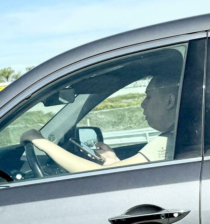 Driver distracted by phone while driving a car, example of dumb drivers caught in the act on the road.