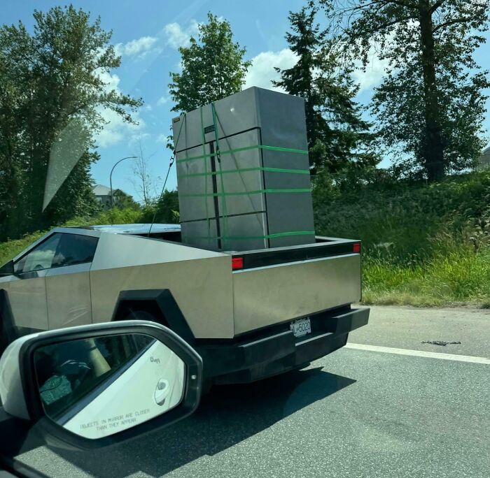 Cybertruck carrying a large unsecured refrigerator on the highway, an example of dumb drivers causing safety concerns.