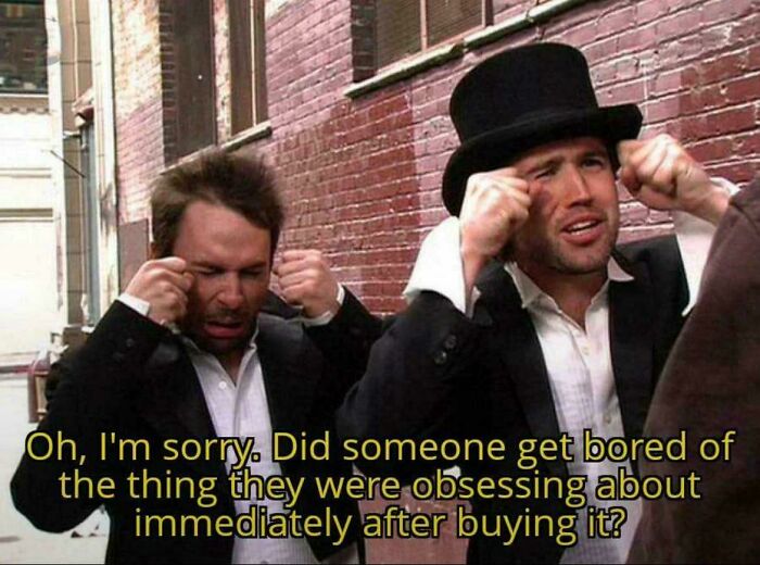 Two men in suits pretending to cry with text highlighting consumerism obsession and boredom after buying items.