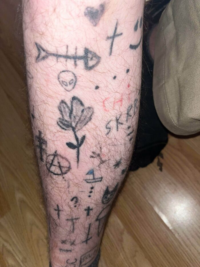 Leg hairy leg covered in numerous small, poorly done tattoos including a flower, alien head, and crosses showing bad tattoos.