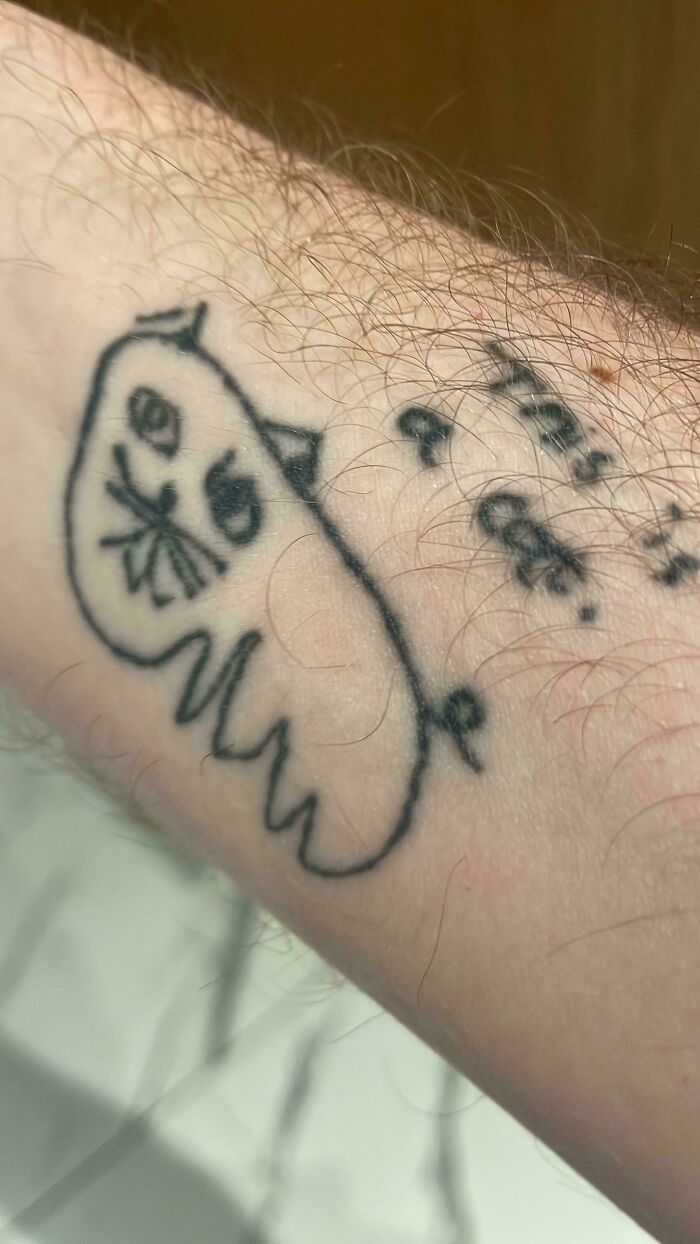 Poorly drawn black ink tattoo of a ghost on a hairy forearm, showing an example of bad tattoos and lack of thinking.