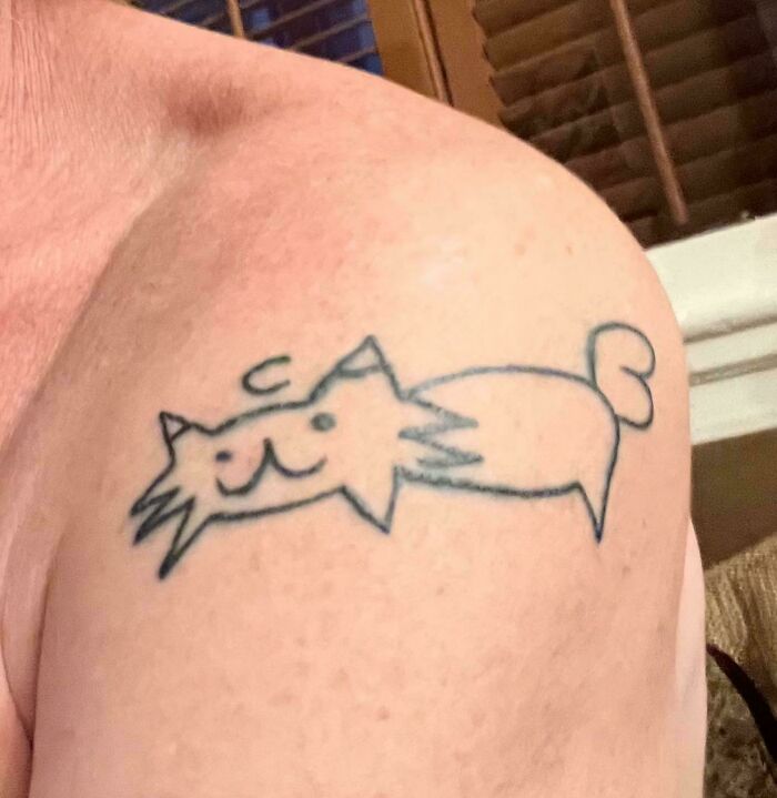 Simple black line tattoo of a poorly drawn cat on a person's shoulder, showing bad tattoos that lacked prior thinking.