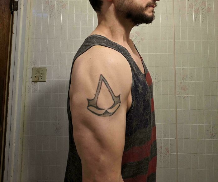Man with a poorly executed tattoo on upper arm wearing sleeveless shirt in a bathroom, showing flawed ink design.