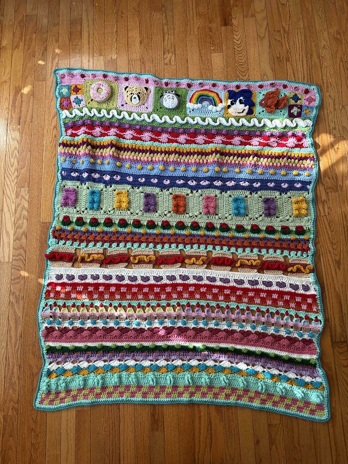 A colorful, intricate crocheted blanket with various patterns, including animals, a rainbow, and hot dogs, showcasing awesome crocheted work.
