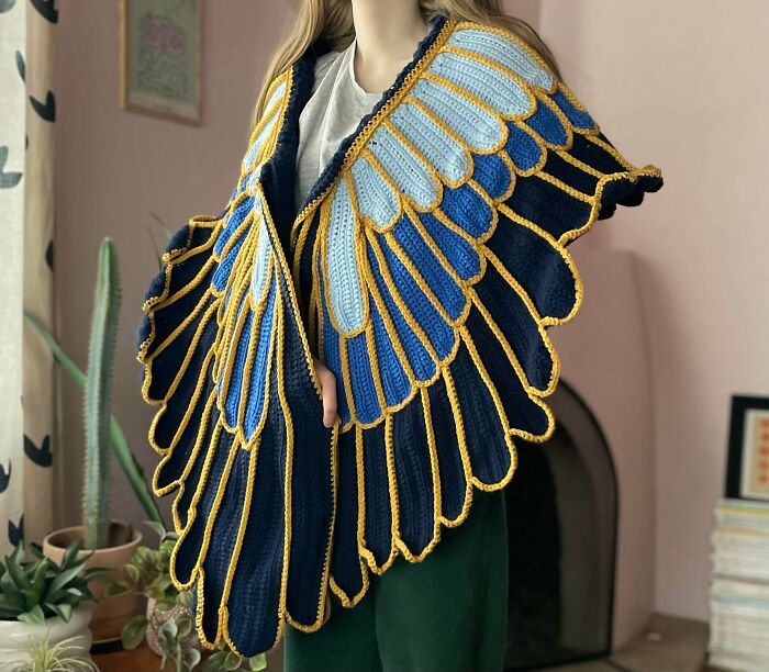 A person models a gorgeous blue and yellow crocheted garment shaped like wings, an awesome crocheted creation.