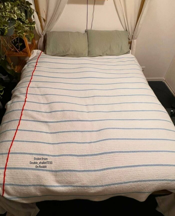 A beautifully crocheted white blanket with blue stripes and a red trim covers a bed. This awesome crochet project wowed the internet.