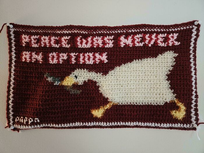 Awesome crocheted piece featuring a goose with text "PEACE WAS NEVER AN OPTION" on a burgundy background.
