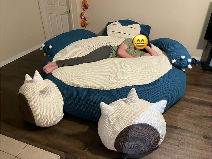 Person relaxing on a giant crocheted Snorlax bean bag, with smaller crocheted pieces next to it. Crocheted something awesome!