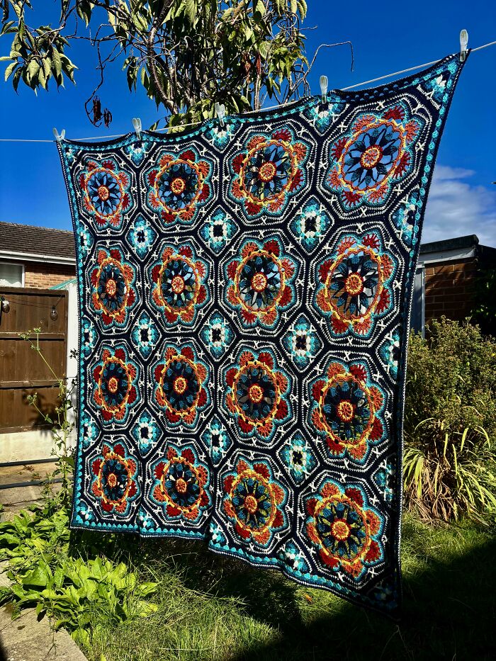 Awesome crocheted blanket with intricate floral designs, drying outdoors. A beautiful example of crocheted art.