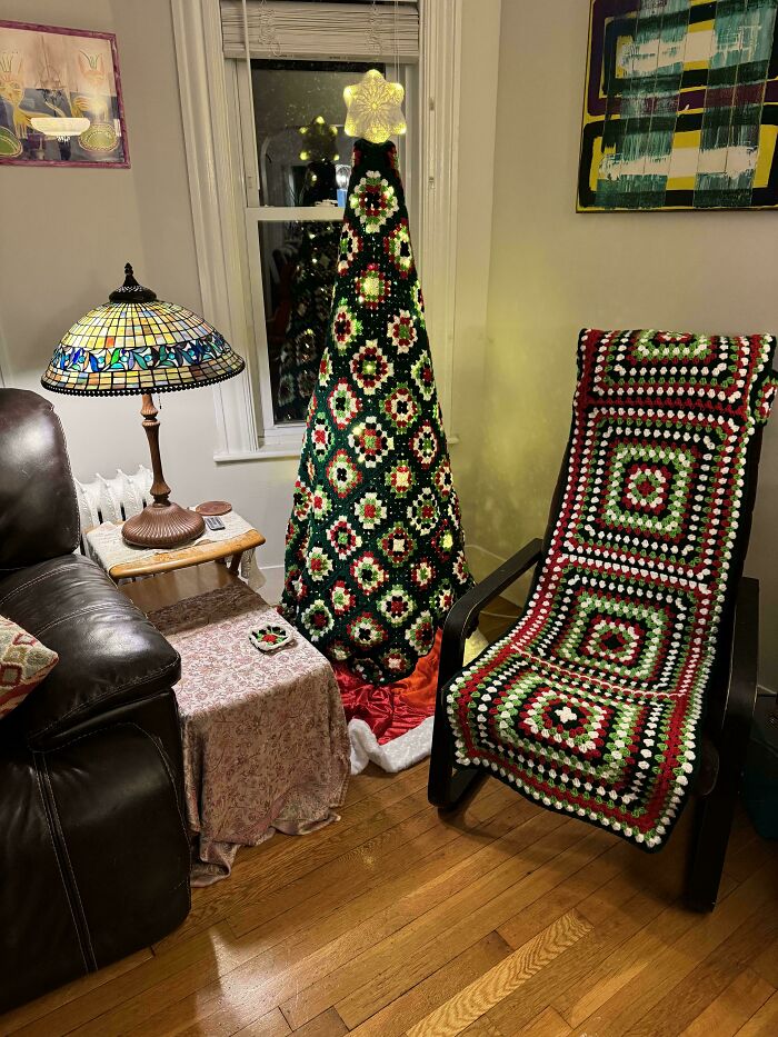A living room with a unique crocheted Christmas tree and matching granny square blanket draped over a chair, awesome crochet.