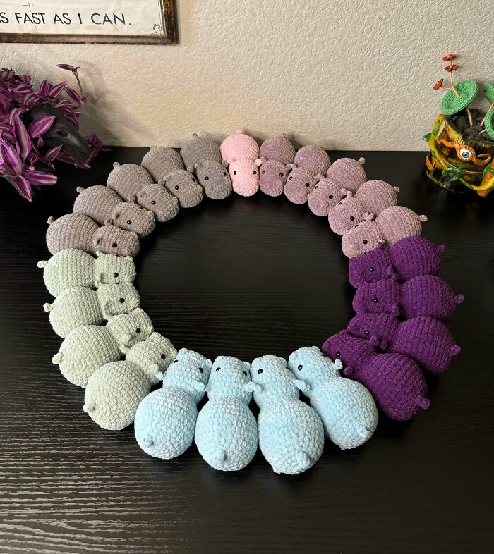 A vibrant circle of crocheted hippos in shades of gray, pink, purple, green, and blue, showing awesome crochet skills.