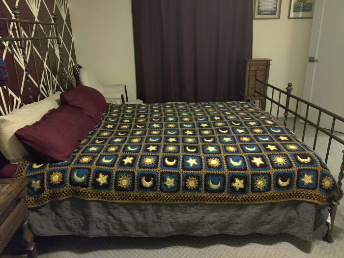 A stunning crocheted blanket with celestial patterns (suns, moons, stars) on a bed, an awesome example of crocheted craft.