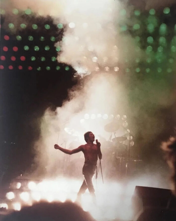 An amazing photo of a shirtless singer on stage, illuminated by spotlights and smoke.