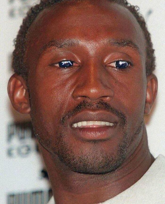 A man with a subtle smile and dark, unusual reflections in his eyes, hinting at a creepy image.