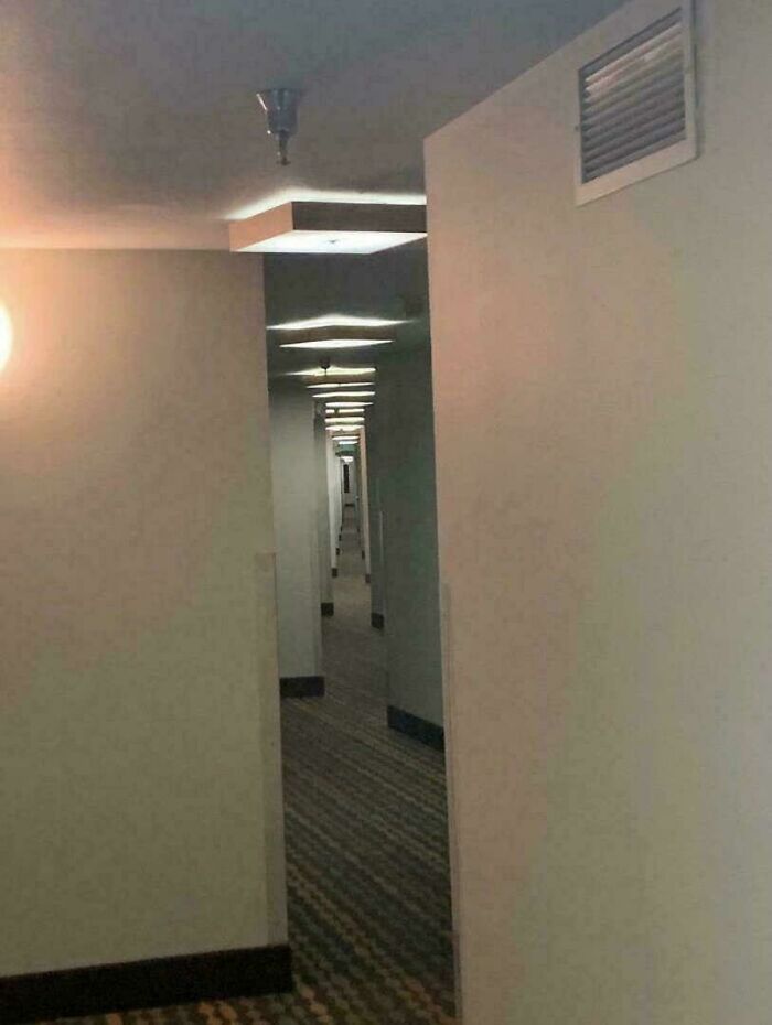 A long, dimly lit hotel corridor with a repetitive pattern on the carpet and glowing recessed lighting. Creepy image for "Hair Of Kids I Babysit".