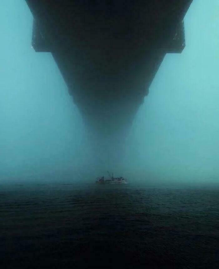 A small boat appears in the distance under a massive, looming structure, creating a creepy image on the water.
