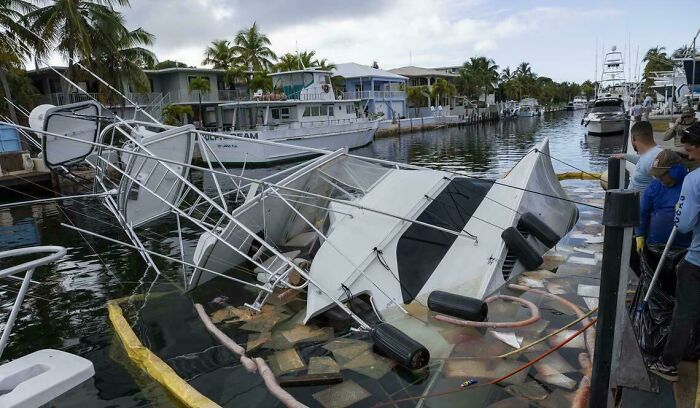 A partially submerged boat after an accident, with debris and rescue workers nearby. Looks expensive.
