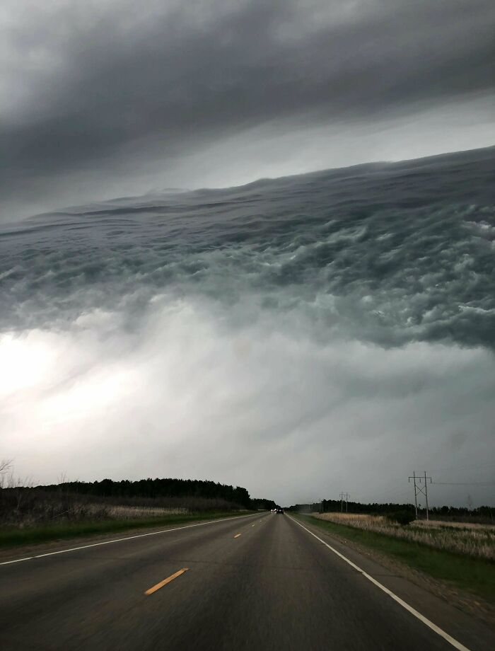 An extremely large and scary shelf cloud over a road, creating an eerie atmosphere with this large thing.