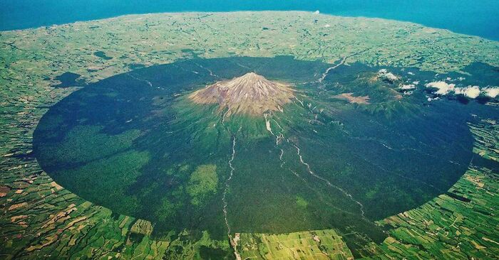 An aerial view of an extremely large, eerie circular forest surrounding a mountain, a large thing.