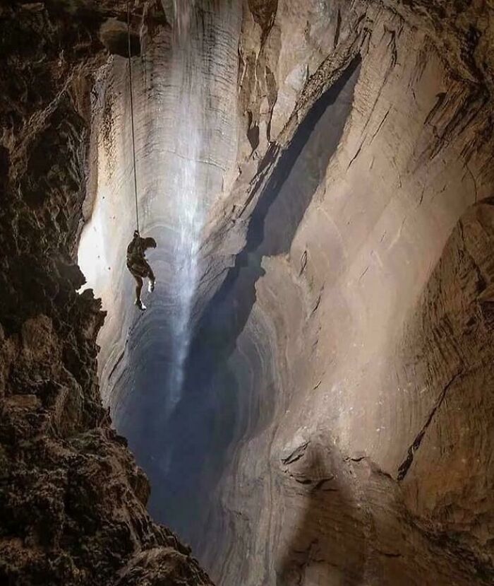A person rappels down into an extremely large, scary, and eerie cave, illuminated by a faint light source.