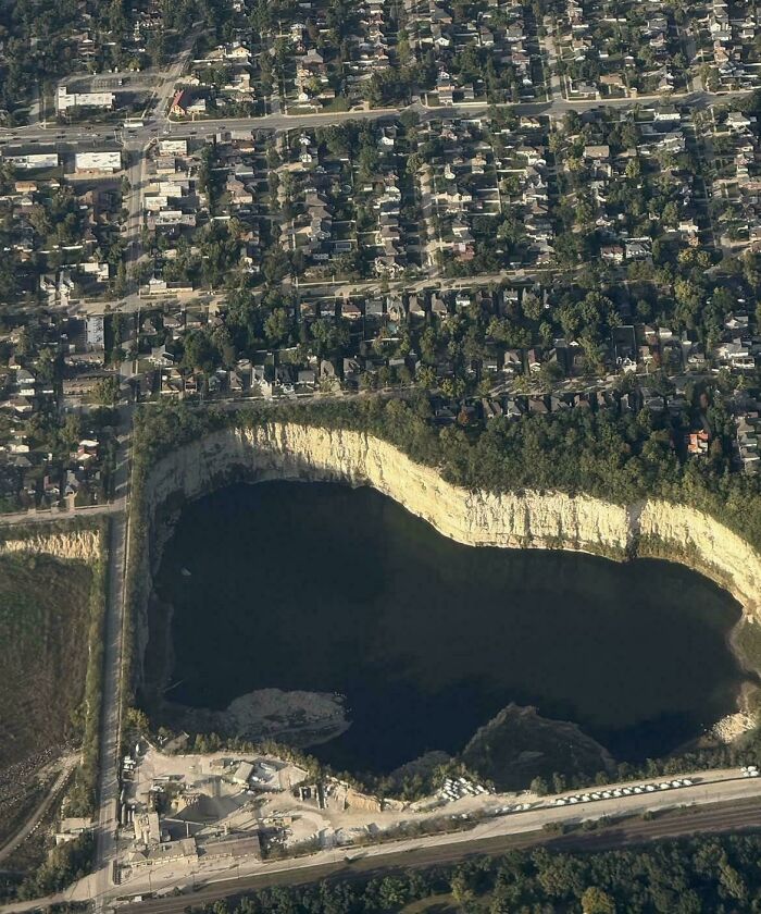 Extremely large things: An aerial view of a vast, scary, and eerie quarry or sinkhole beside a densely populated suburban area.