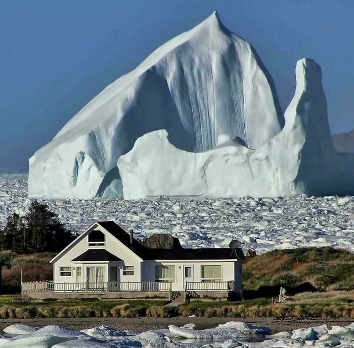 Extremely large things: A tiny house dwarfed by a huge, scary, and eerie iceberg in a frozen landscape.