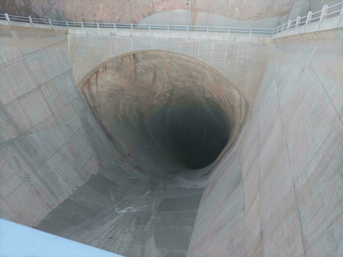 Extremely large things: A deep, eerie, and scary concrete spillway, appearing as a massive void in a dam structure.