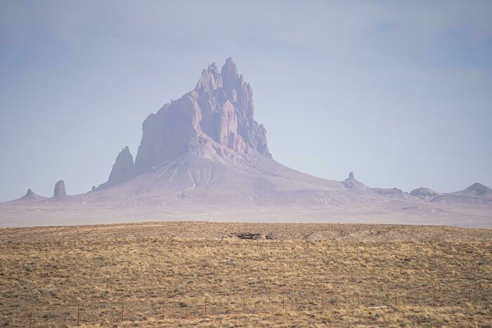 An extremely large, jagged mountain peak rising from a vast, flat landscape, an eerie and scary natural formation.