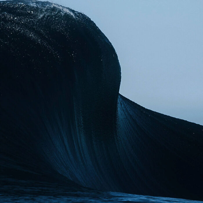 A massive, dark wave cresting, an extremely large thing that appears scary and eerie against the sky.
