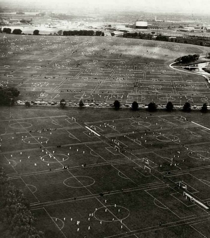 Aerial view of numerous soccer fields showing extremely large things and eerie scale with distant buildings.