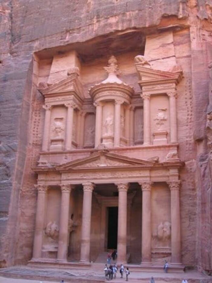 An extremely large ancient stone building carved into a cliff face, showing scary and eerie human scale.