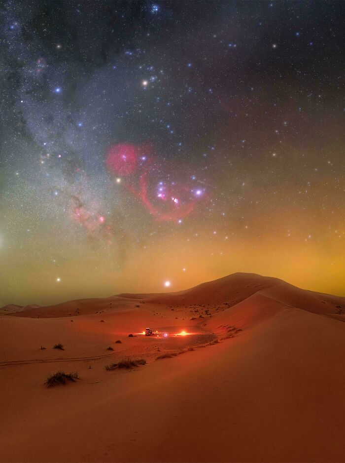 Extremely large desert dunes under a starry, eerie night sky, with a small camp showing the scary vastness of nature.