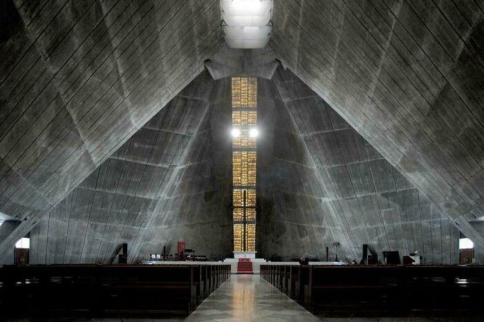 Extremely large and eerie concrete church interior with a cross-shaped stained-glass window, creating a scary sense of vastness.