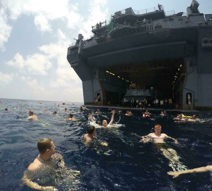 Extremely large ship with people swimming in the ocean nearby, showing the scary scale of the vessel and eerie vastness of the sea.