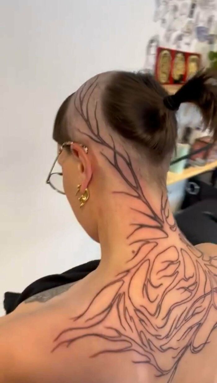 A woman with an intricate back tattoo and a shaved neck, showing an unfortunate haircut.