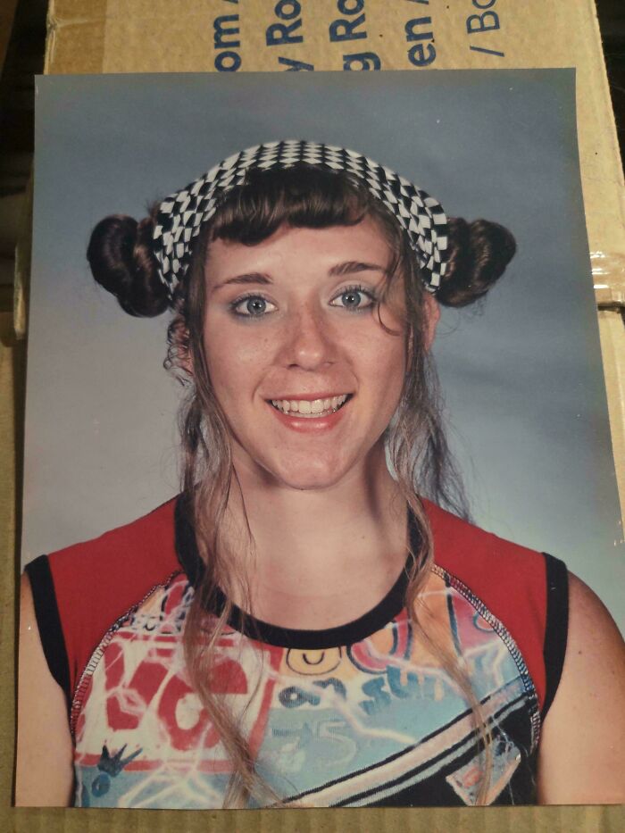 A woman with a black and white checkered headband, pigtails, and an unfortunate haircut, smiling at the camera.