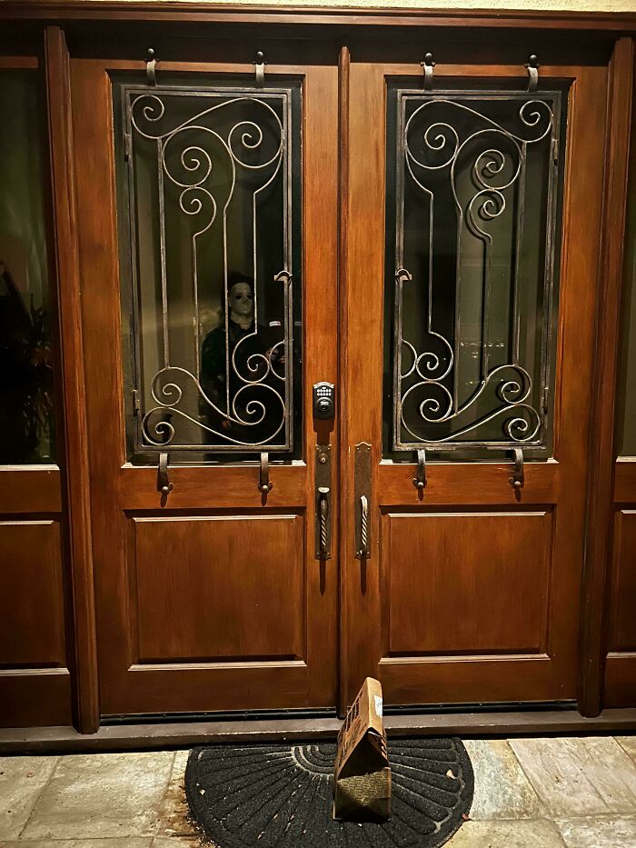 Package left outside front door with spooky figure visible inside through decorative glass in a hilarious delivery confirmation pic.
