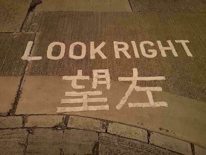 Sidewalk painted with a you had one job fail showing conflicting directions to look right and left in English and Chinese.