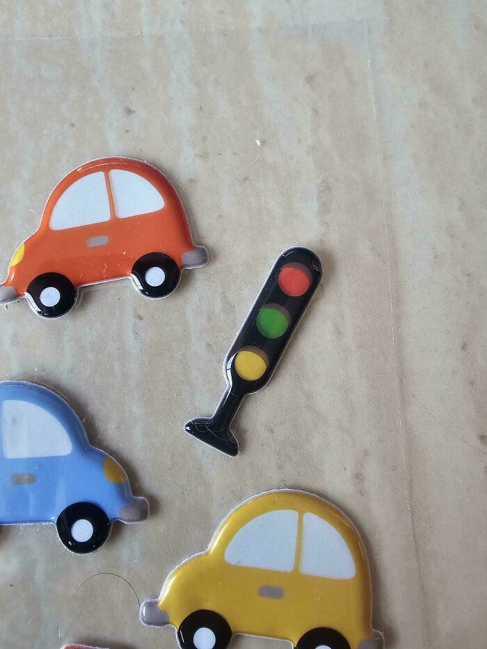 Toy traffic light with red, yellow, and green lights positioned incorrectly among colorful toy cars, illustrating common sense fails.