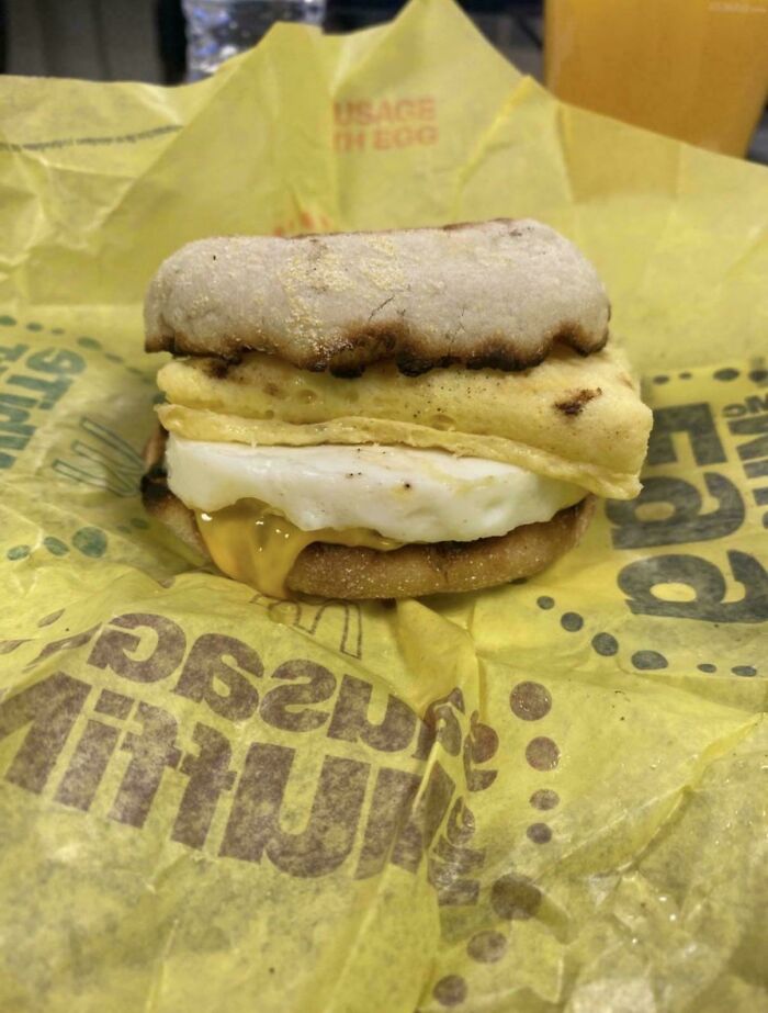 Breakfast sandwich with burnt English muffin and unevenly folded egg on fast food wrapper, showing job fail example