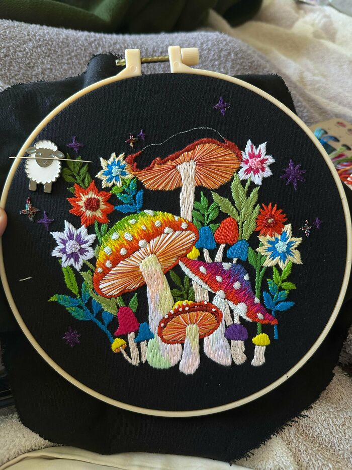Vibrant and stunning embroidery creation in a hoop, showcasing colorful mushrooms and flowers on black fabric, inspiring hobby.