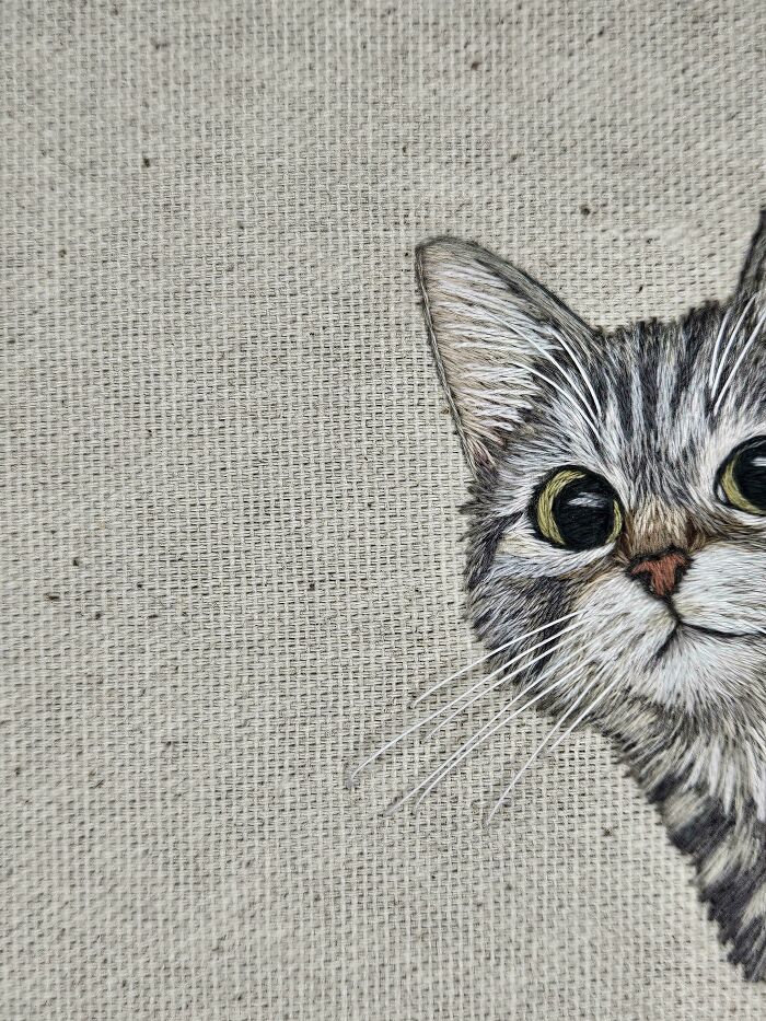 Close-up of a stunning embroidery creation depicting a grey tabby cat peeking from the side, a creative hobby.